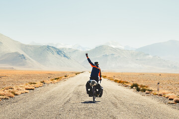 Back view adventurous caucasian male traveller cycle bicycle touring solo on asphalt famous Pamir highway M41 road in remote high Pamir mountains. Pamir highway adventure travel route destination