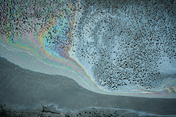 Colorful gasoline or oil spill creating a rainbow sheen on a wet asphalt surface after rain,...