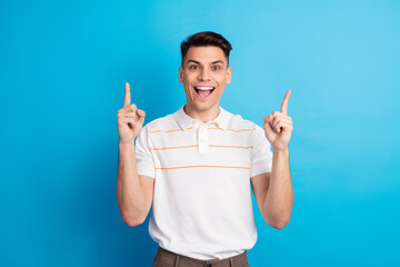 Young man gesturing happily with both hands up while standing against a vibrant blue background in...