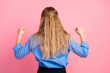 Back view of a young girl with blonde hair showing victory gesture against a pink background...