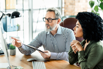 Mature businessman and female colleague discussing a project in a modern office environment with...