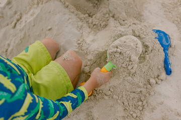 Child playing in sand at a beach, building a sandcastle with colorful tools during sunny summer day