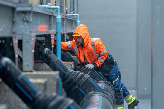 Factory worker or technician with raincoat check and maintenance pipe system in area of factory building during raining.