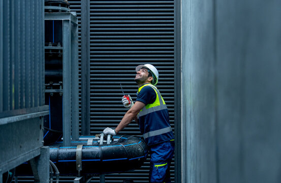 Medium shot of engineer or technician worker hold  walkie talkie and stand with looking and maintenance during work with steel pipe system of factory building.