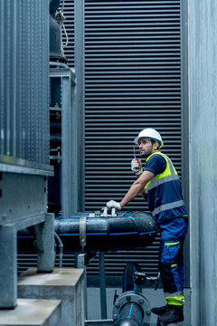 Vertical image of engineer or technician worker hold  walkie talkie and stand with looking and maintenance during work with steel pipe system of factory building.