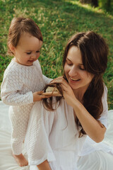 Happy young mother playing with her baby on the grass in a sunny park. Family bonding, early...