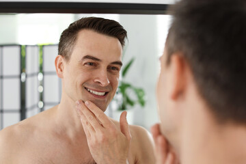 Smiling man after shaving looking at mirror in bathroom