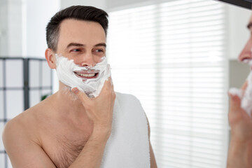 Smiling man applying shaving foam near mirror in bathroom