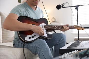 Man working with guitar and MIDI keyboard on sofa in home studio, closeup