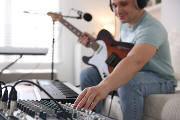 Man working with guitar, dj mixer and MIDI keyboard on sofa in home studio, selective focus