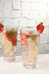 Tasty refreshing drink with strawberries, lemon and mint on white table