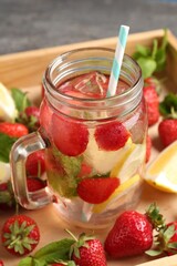 Refreshing drink with strawberries, lemon and mint in mason jar surrounded by fruits in wooden crate on grey table, closeup