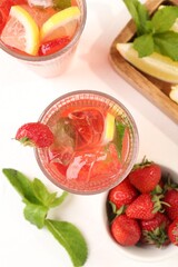 Refreshing drink with strawberries, mint, lemon and ice on white table, flat lay