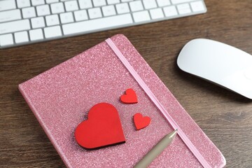 Decorative hearts, computer keyboard, mouse, notebook and pen on wooden table, above view. Online...
