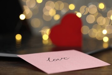 Online dating site. Sticky note with word Love, decorative heart and laptop on table, closeup....