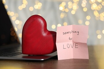 Online dating site. Sticky note with text Searching For Love, decorative heart and laptop on wooden...