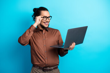 Young professional man holding a laptop confidently against a vibrant turquoise background, exuding...
