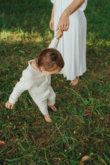 Happy young mother playing with her baby on the grass in a sunny park. Family bonding, early...