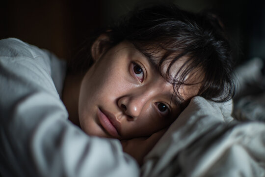 Close-up portrait of a young woman lying down with a tired and contemplative expression in dim light