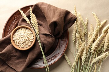 Many wheat spikes, plate, napkin and seeds on paper background, flat lay