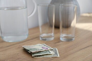 Tips, glasses and jug of water on wooden nightstand in hotel room, closeup