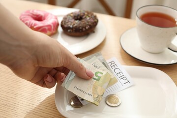 Woman putting tips onto plate at wooden table in cafe, closeup