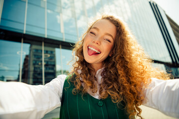 Stylish woman in green vest enjoying a sunny urban day outdoors with a playful and joyful expression