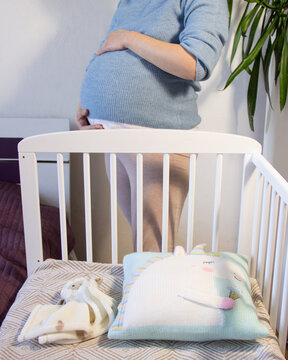 Pregnant Woman Touching Belly Next to Crib in Baby Room