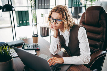 Businesswoman in an office wearing formal attire works on a laptop displaying a bored expression...
