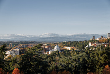 Fototapeta premium View of a cityscape with autumn foliage and distant mountains during a clear day near an urban park