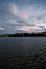 Cloudy sunset over calm waters near scenic hills in a tranquil natural setting