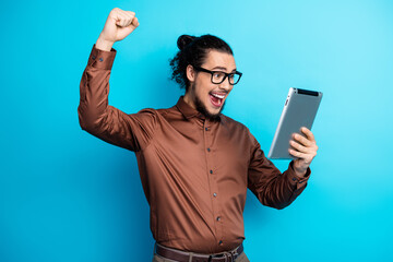 Handsome young man celebrates success while holding digital tablet against a vibrant turquoise...