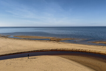 Calm shoreline landscape featuring a lone figure walking along a sandy beach by the water in a serene coastal setting