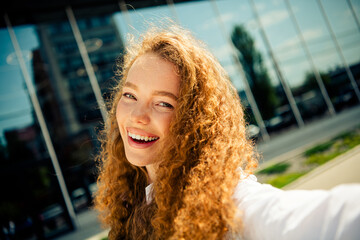 Young professional woman with curly red hair enjoying sunny day outdoors near urban office building