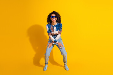Fashionable young woman with sunglasses posing confidently against a vibrant yellow background...