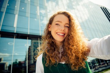 Confident curly-haired businesswoman poses outdoors with a stylish waistcoat against modern city...