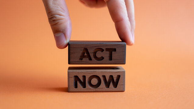 A hand places a wooden block with the word act on top of another wooden block with the word now