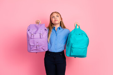 Smiling girl holding two backpacks making choices on a pink background