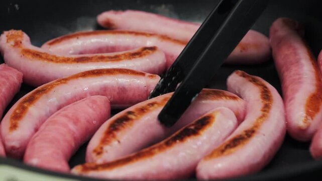 Meat sausage on a pan grill close-up. Traditional fast food. Flipping sausages in a frying pan. High quality 4k footage