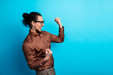 Excited young businessman in stylish brown shirt celebrating success with punch gestures against a...