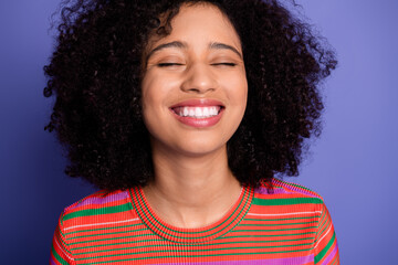 Joyful young woman with curly hair and a vibrant striped shirt smiling against a purple background