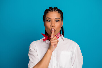 Young woman with braided hair making silence gesture wearing white shirt and red scarf on blue...