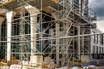 Construction Site In Freiham Munich Bavaria: Large Building Foundation With Concrete Structures, Yellow Cranes, Steel Framework, And Urban Housing In Background Under Partly Cloudy Sky