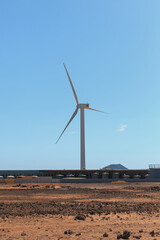 A tall wind turbine stands prominently at a coastal location, harnessing wind energy against a...