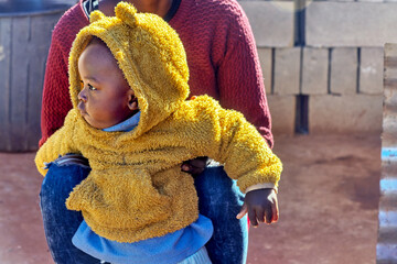 African village, single happy africa kid held by his mother outdoors in the yard walking in the...