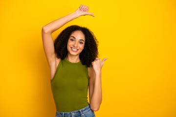 Attractive young woman pointing and smiling in stylish casual clothing against a vibrant yellow...