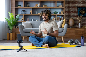 A man is giving a speech while on a video call, sitting on a yoga mat in his living room.