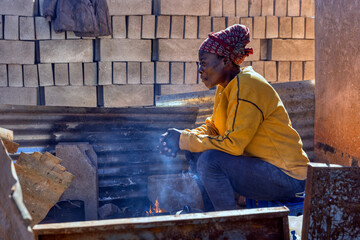 African village, africa woman sitting next to the fire in the yard resting in a sunny morning