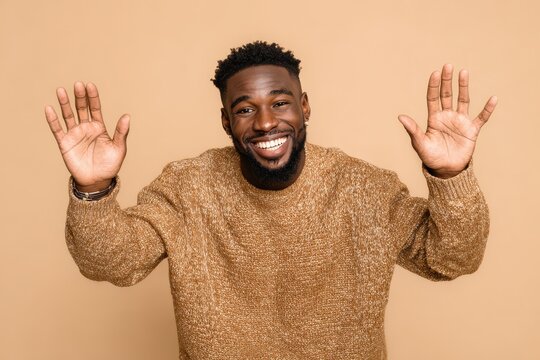 An African American man in a plain setting smiles at the camera with open arms radiating joy