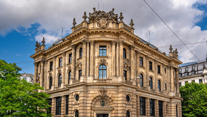 Fototapeta premium Baroque Architecture In Munich: Ornate Historic Building With Sculpted Facade, Arched Windows, Decorative Columns, And Stone Details Under Blue Sky With Clouds In Vibrant Urban Cityscape